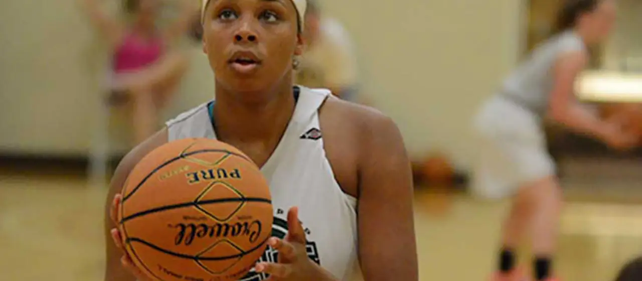 Female athlete focuses on free throw shooting routine during basketball camp training session.