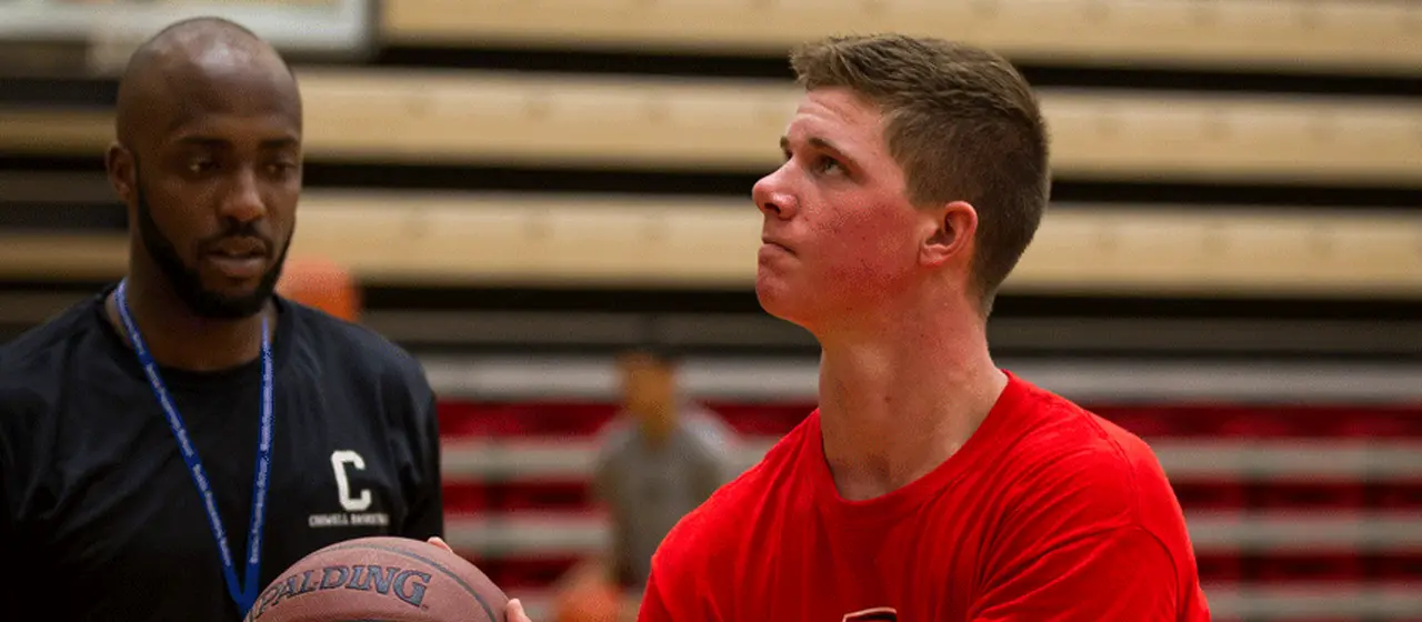 Coach helps correct basketball player working on his shooting.