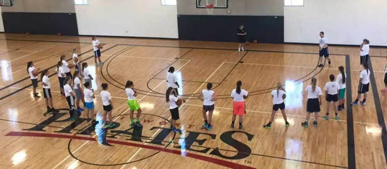 Athletes watch coaches demonstrate basketball drill.